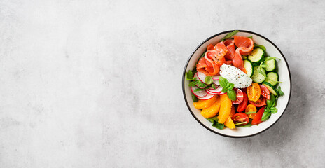 Salmon bowl with spinach,arugula, cherry tomatoes, cucumber, orange slices, radish and cream cheese. Homemade food. Concept for a tasty and healthy meal. Light gray stone background. Top view.