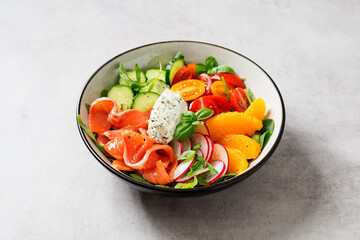 Salmon bowl with spinach, arugula, cherry tomatoes, cucumber, orange slices, radish and cream cheese. Homemade food. Concept for a tasty and healthy meal. Light gray stone background. 