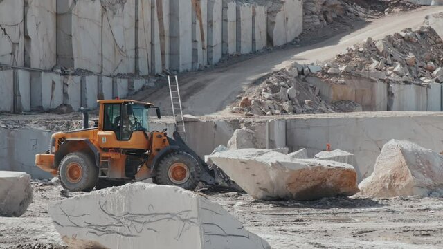 Slowmo shot of unrecognizable worker operating loader and transporting granite block in quarry