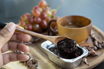 Hand holding a spoon scooping brown cakes and coffee and grapes on a wooden floor.