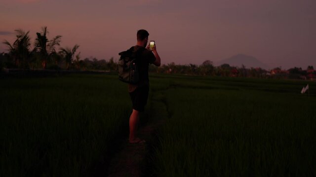 Video of caucasian man in casual wear walking in evening dusk on wild nature destination using mobile phone for taking picture of environment, male influencer making media content during trip
