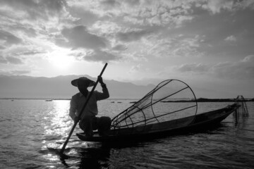 loacal asian fisherman sitting on boat while catching fish in morning at inle lake. monochrome color