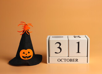 wooden calendar 31 October and Halloween witch hat decorated with pumpkin head and spider on orange...