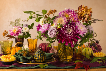 Fototapeta na wymiar Festive table setting for Thanksgiving day. Autumnal decorations,plates, multicolor glasses and beautiful garden flowers.