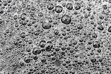 Gentle white foam with bubbles pattern on dark water surface after heavy rain as decorative background close view from above