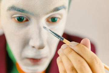 Mim is preparing makeup for performance. Close up of clown cosplayer. Guy with green hair in...