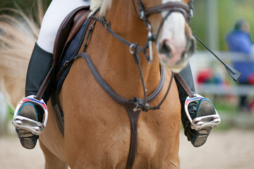 Croup of a red horse with a saddle and a rider’s foot in a boot with a spur inserted in a stirrup.