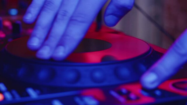 Hand rotates round platform on digital mixing console while one track is playing to adjust speed of second track, closeup. Concept of DJ professionalism