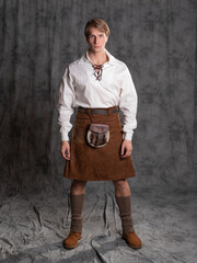 A young man in a leather kilt and a white lace-up blouse. A Scottish knight - obrazy, fototapety, plakaty
