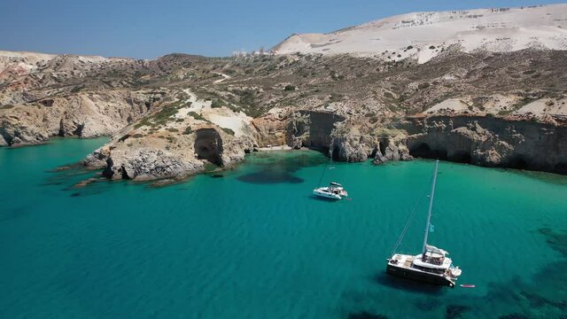 Aerial drone video of beautiful scenic rocky cove and beach of Tsigrado with caves and crystal clear emerald sea, Milos island, Cyclades, Greece