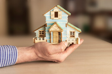 The concept of mortgage and rental housing and real estate. Mortgage credit lending. The layout of a wooden house in the hands of a man.