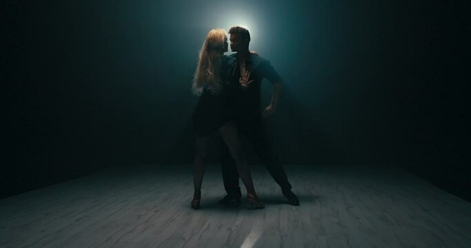 Couple in love training choerography dance bodies close together slow sexy seductive female movements man touches girl's body buttocks thighs turns her hips blonde is wearing cabaret high heels