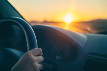 Female hands of car driver on steering wheel, road trip at sunset