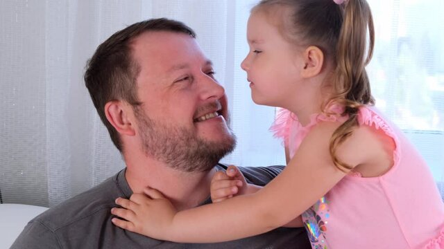 little daughter, 3 years old, tells her dad a secret, play together at home. Father's day. Handsome young man at home with his little cute girl are having fun together. Fatherhood concept, happy