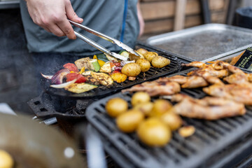 A chef with tongs overturning some vegetables on a grill surface