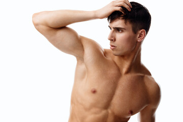 Fototapeta premium confident man athlete with a pumped-up torso touches his head with his hand on a light background