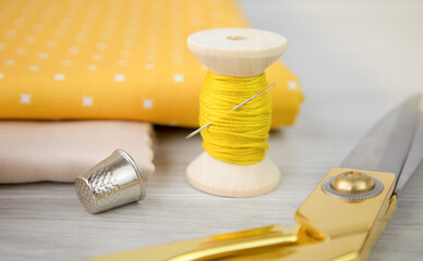 a spool of yellow thread, a cotton cloth and a thimble on the table.Sewing accessories