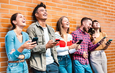 Multicultural friends laughing using smartphone at wall on university college campus - Young people addicted by mobile smart phones - Technology concept with always connected milenials - Vivid filter - obrazy, fototapety, plakaty