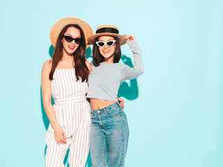 Two young beautiful smiling hipster female in trendy summer white t-shirt and jeans clothes.Sexy carefree women posing near light blue wall in studio.Positive and cheerful models in hats