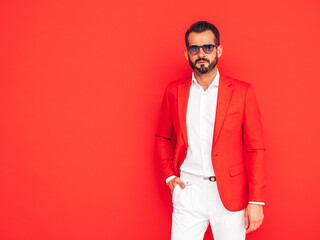 Portrait of handsome confident stylish hipster lambersexual model. Sexy modern man dressed in elegant suit. Fashion male posing in studio near red wall in sunglasses