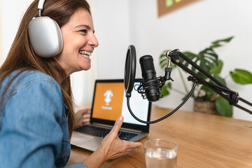 Host woman recording a podcast using microphone and laptop from her home studio