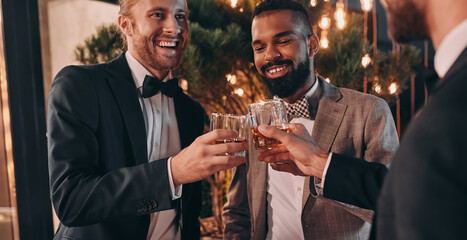 Three well-dressed men drinking whiskey and communicating while spending time on party