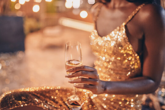 Close-up of beautiful young African woman in evening gown holding flute with champagne