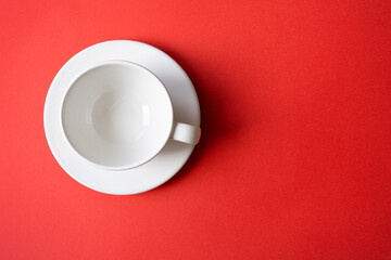 Simple flat lay composition with empty white ceramic cup, mug, bowl on a plate with bright red background, top view, space for text