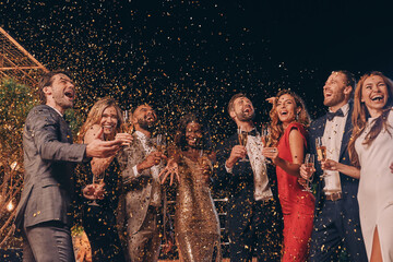Group of happy people in formalwear having fun together with confetti flying all around
