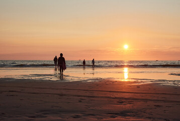 A silhouette of people walking on a sea shore at sunset