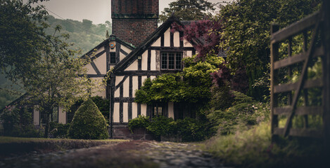 Old fashioned Tudor vintage home along a gravel driveway behind a gate - obrazy, fototapety, plakaty