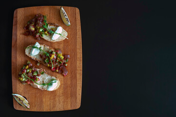 Bruschetta with fresh tuna tartare with avocado and cucumber on a wooden board on a black background. copy space.