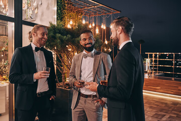 Three well-dressed men drinking whiskey and communicating while spending time on party