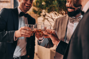 Close-up of three well-dressed men drinking whiskey and communicating while spending time on party