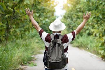Back view of male traveler standing on the road to the forest, raises his arms up. Concept : Eco traveling. Recreation on holiday. Trekking in the forest alone. Survival in forest. Copy space    
