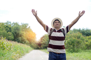 Fototapeta premium Back view of male traveler standing on the road to the forest, raises his arms up. Concept : Eco traveling. Recreation on holiday. Trekking in the forest alone. Survival in forest. Copy space 