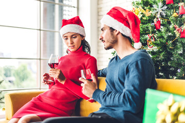Fototapeta premium Romantic sweet couple in santa hats having fun and drinking wine glasses while celebrating new year eve and enjoying spending time together in christmas time at home