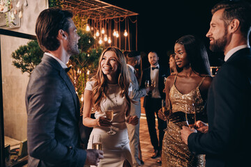 Group of people in formalwear communicating and smiling while spending time on luxury party