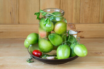 Canning vegetables at home. Salted green tomatoes in a glass jar on a wooden table. Selective focus.