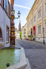 Augustiner Brunnen (Augustinian fountain) in Augustinergasse (Augustinian street), typical fountain in Basel, Switzerland, with national history museum and red Basler M&uuml;nster (Basel minster cathedral)