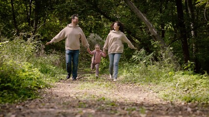 Dad, kid, daughter, mom, are playing in park, run along path holding hands. Happy child is holding hands of parents. Happy family walks in forest holding hands in summer. Teamwork. Family weekend