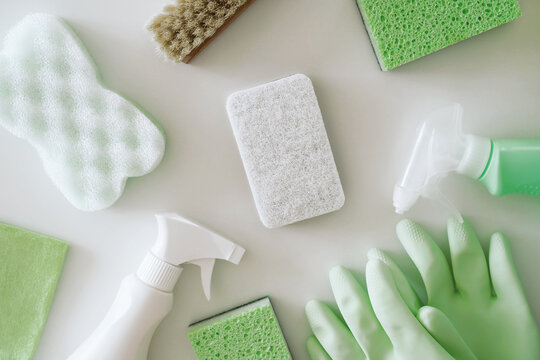 Green protective gloves, sponges, rag, brush, spray cleaner bottle with chemical detergent on white background. Housework and professional eco cleaning service supplies.