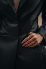 Female hands with silver rings in the pockets of a black long leather jacket. Style, design of women's clothing. Vertical