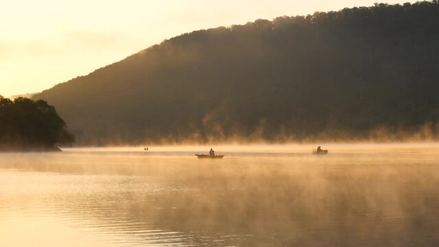 Morning fog on the lake at sunrise, men fishing from a boat, (Edersee, Germany)