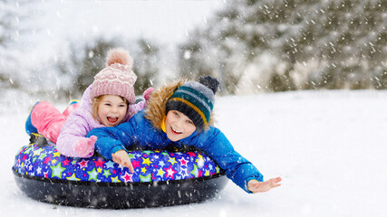 Active toddler girl and school boy sliding together down the hill on snow tube. Happy children,...