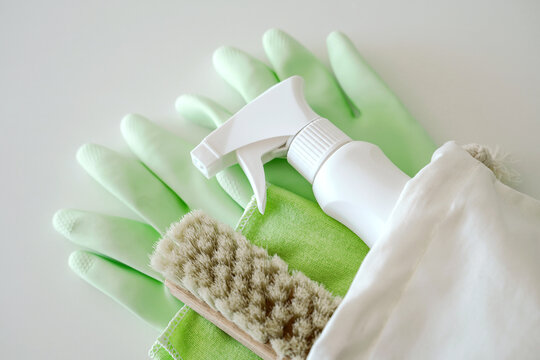 Green protective rubber gloves, rag, brush and sprayer with chemical detergent on white background. Housework and professional eco cleaning service supplies.