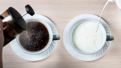 Two cups with pouring milk and black coffee