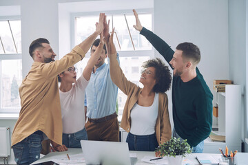 Group of happy young people in smart casual wear holding hands together and smiling