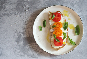Sandwich with cheese, tomatoes and basil on a dessert plate. The top of the sandwich is watered with butter. Top view