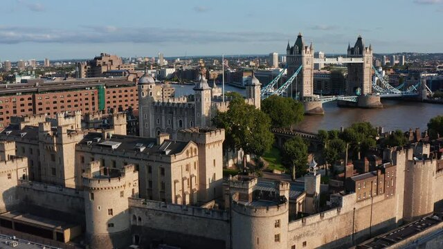 Forwards fly above Tower of London in golden hour. Impressive stone fortification of medieval castle. Old White Tower with four corner towers and Union Jack on pole. London, UK
